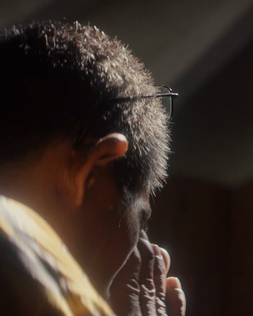 Virgilio from behind in a dark room, his hand to his face.