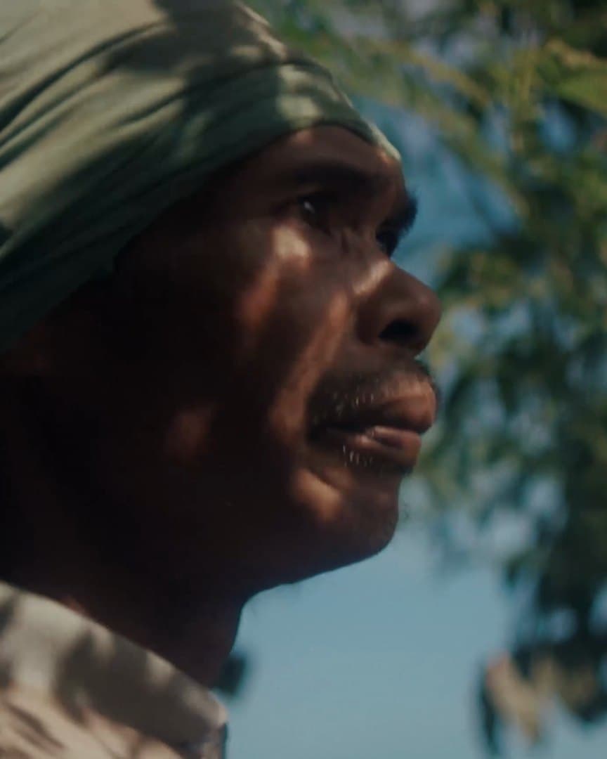 A farmer in a head wrap, looking out across the field.