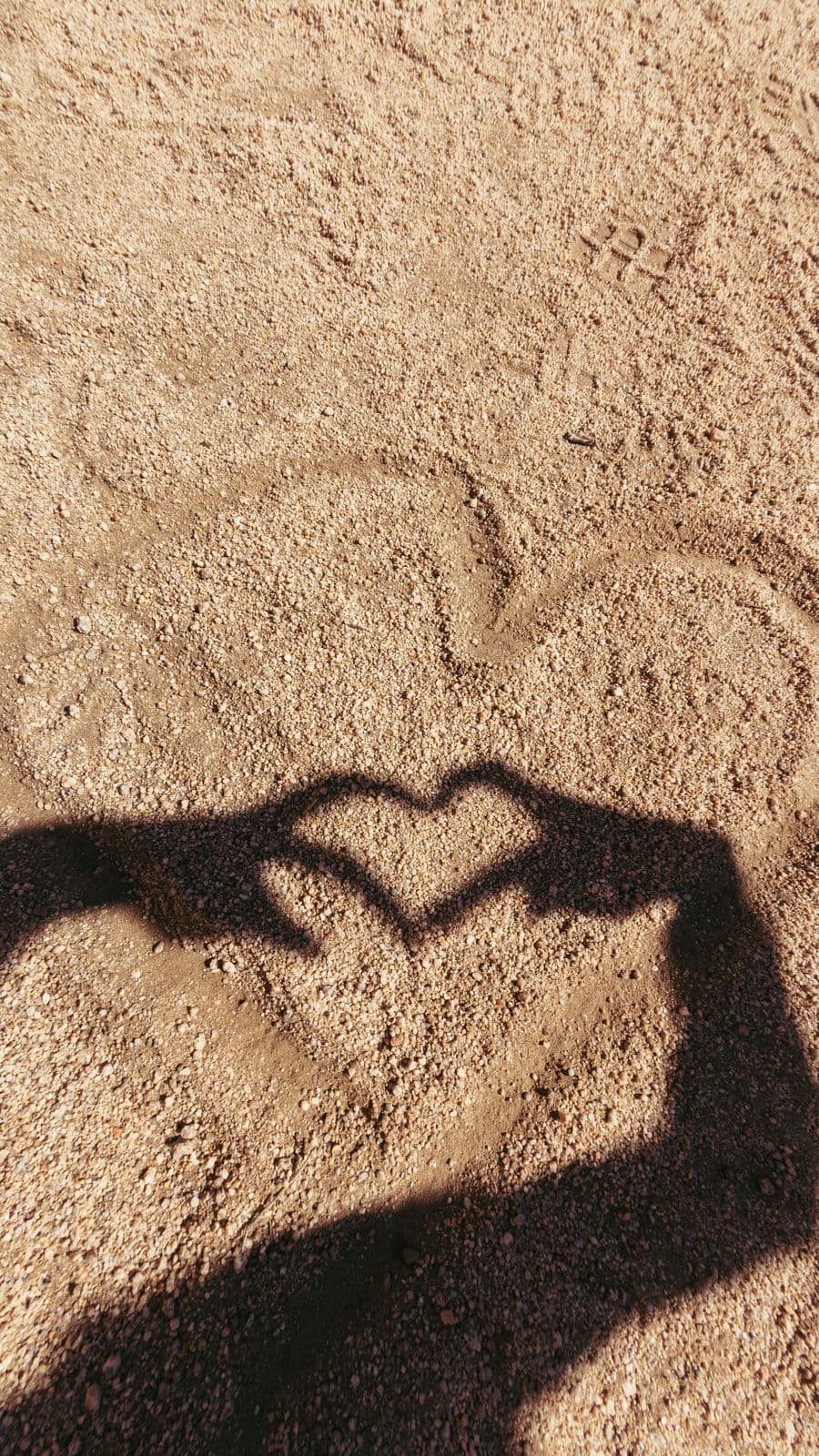 Two hands making a heart in shadow on the sand.