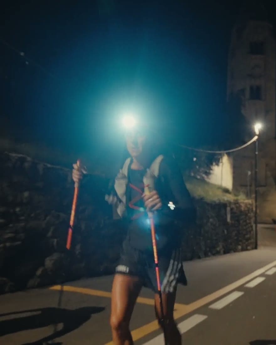 A runner on tarmac at night, headtorch flaring toward camera.