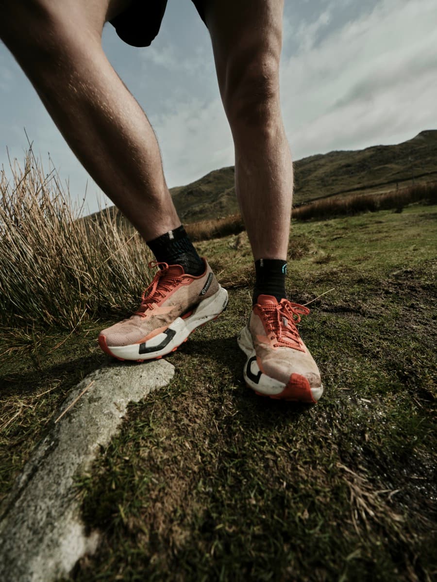 A runner's legs and trail shoes low against the fells, mid-stride.