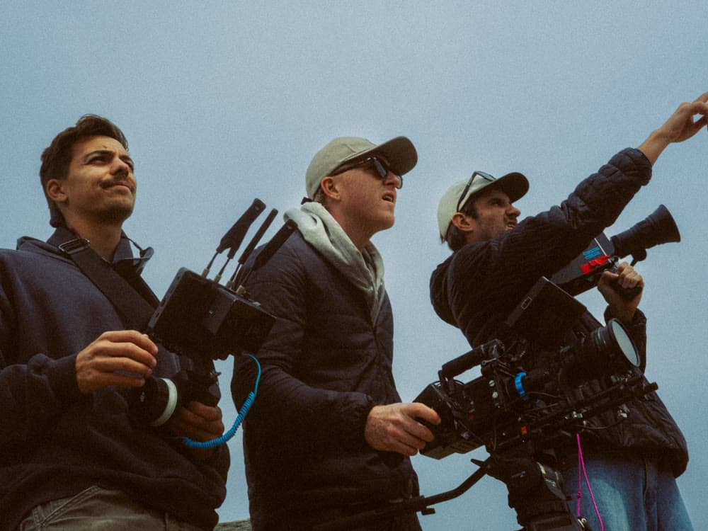 Three crew working cameras against open sky.