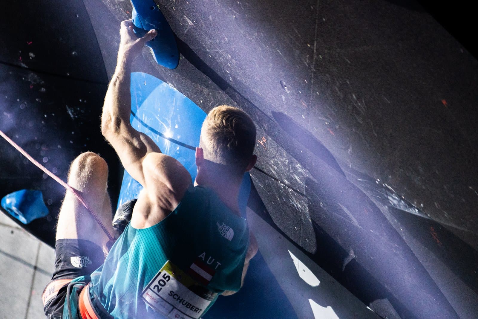 A climber reaching across the wall under violet light.