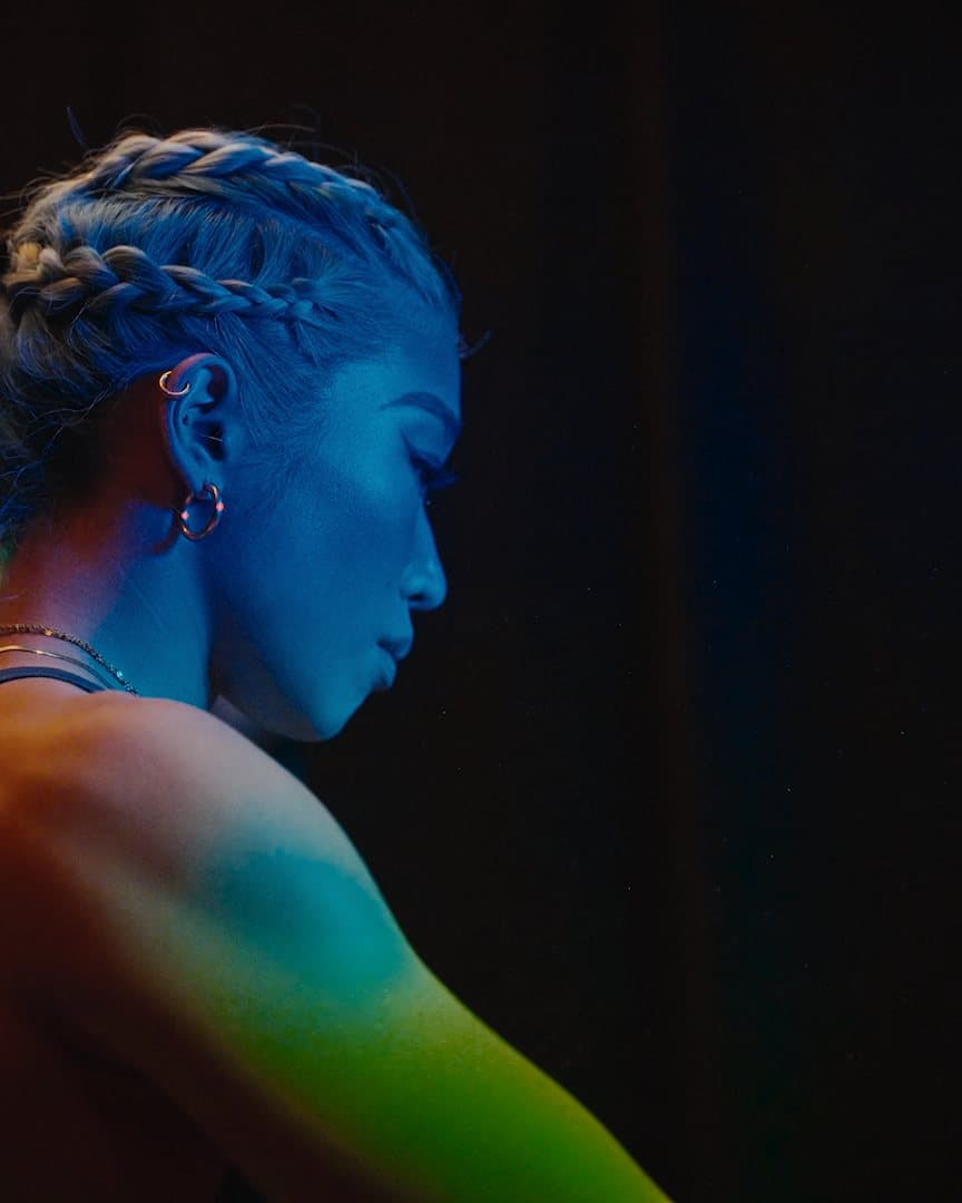 A climber with braided hair in coloured stage light.