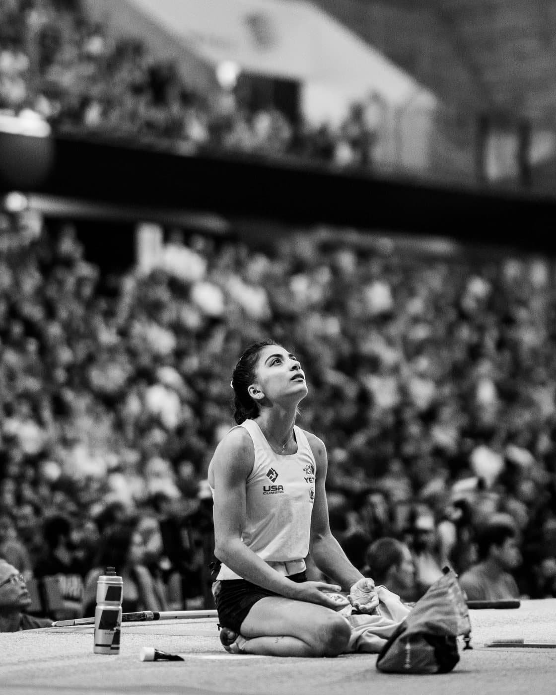 A climber sitting on the mat in front of a packed arena, in black and white.