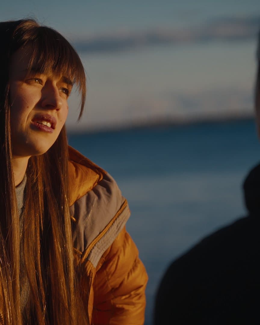 A climber in an orange jacket by the water at dusk.
