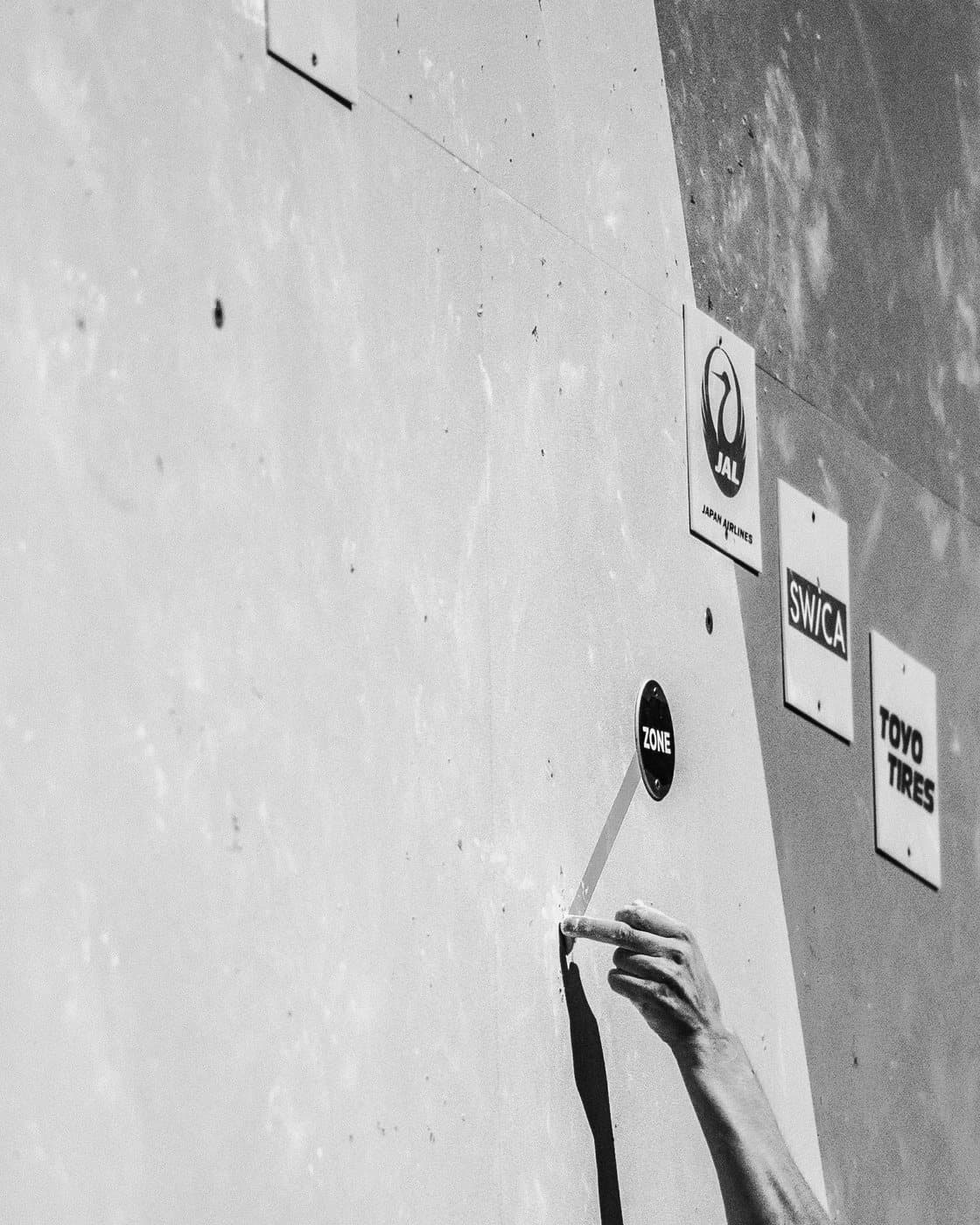 A climber’s arm on a grey wall, in black and white.