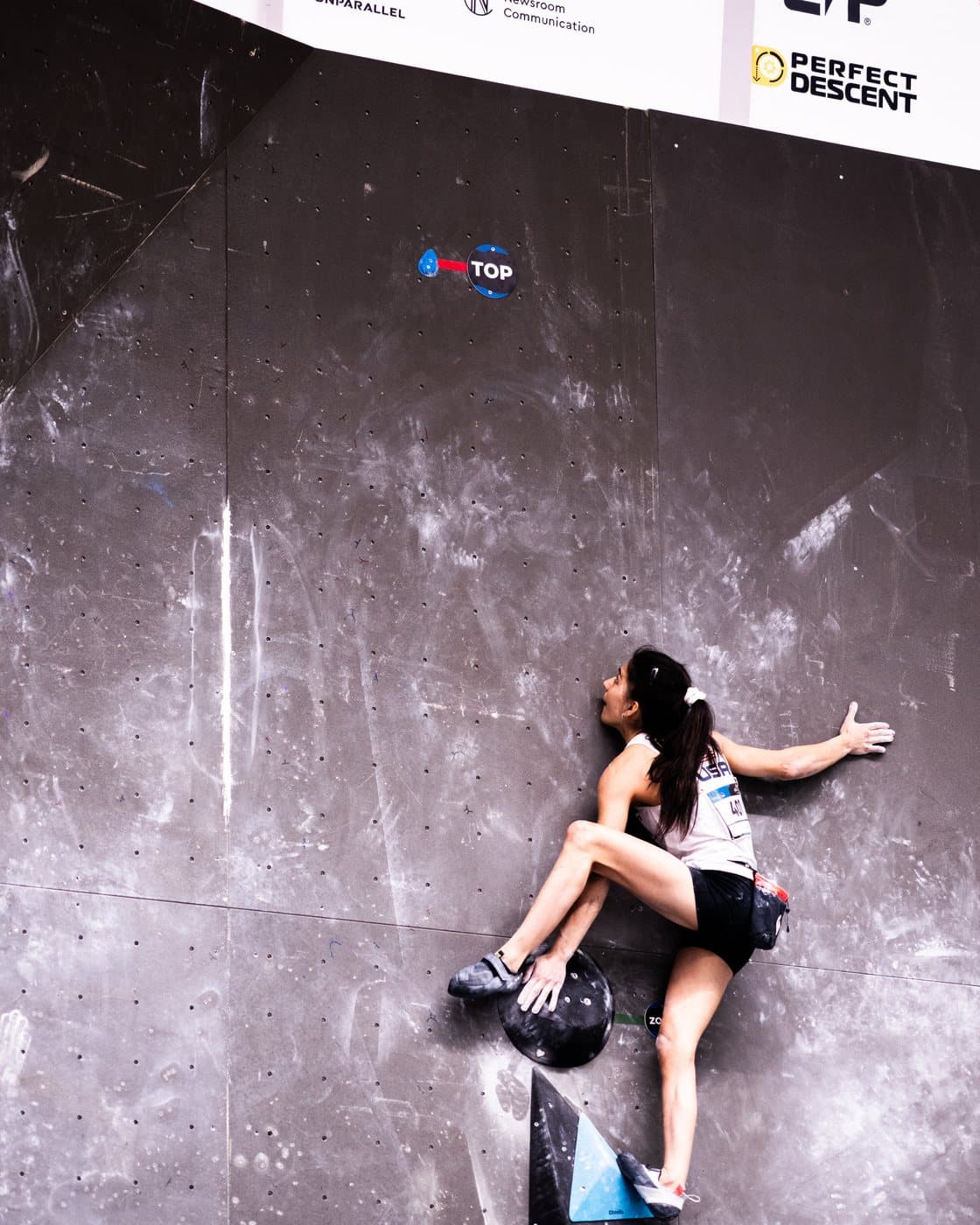 A climber stretching for a hold on a purple-lit wall.
