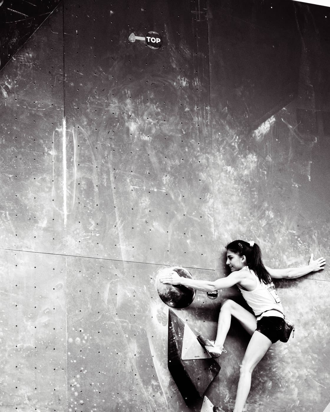 A climber hanging from a hold, from below, in black and white.