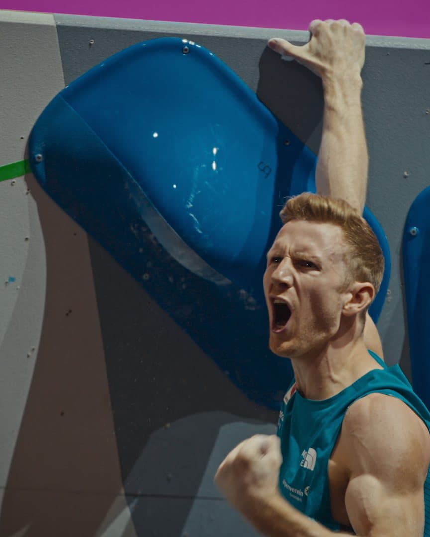 A climber roaring after topping a boulder.