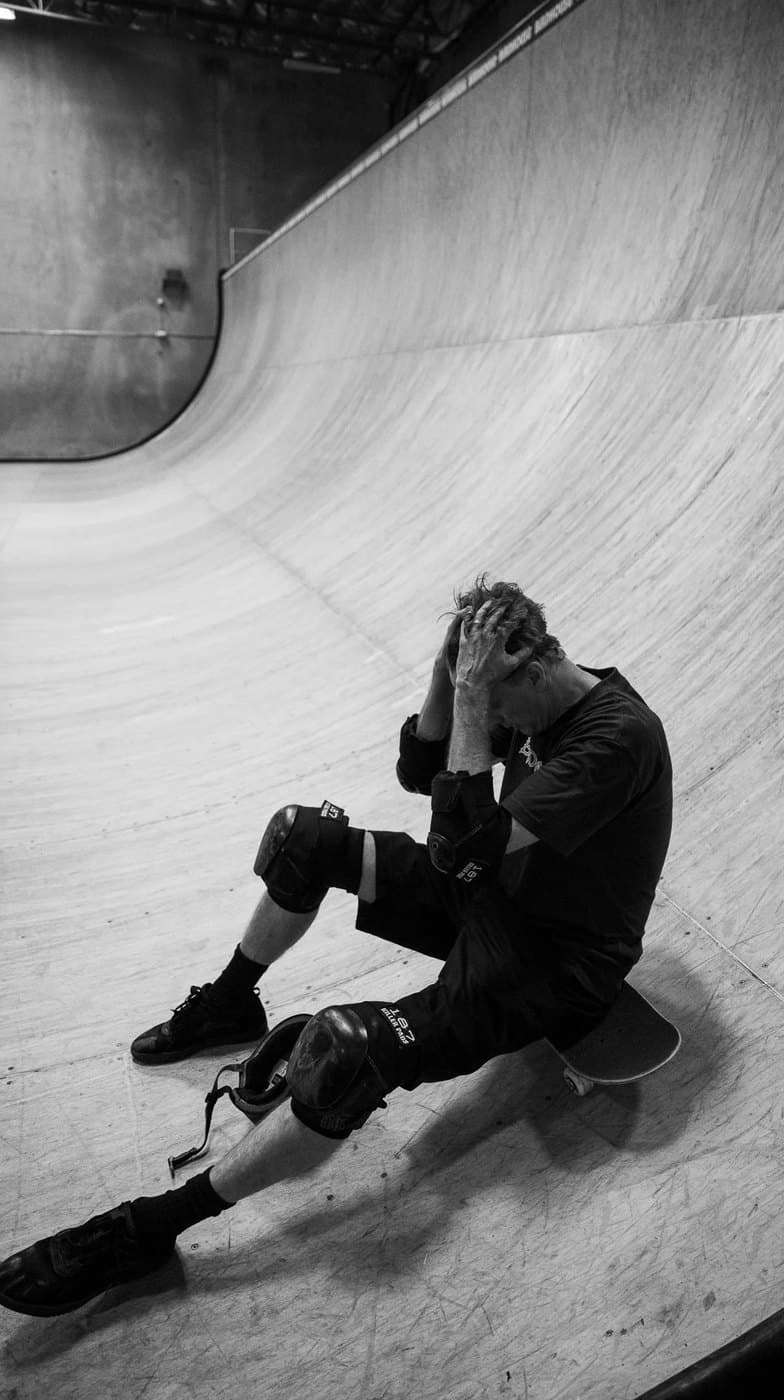 Tony Hawk sitting on the deck of a halfpipe, in black and white.