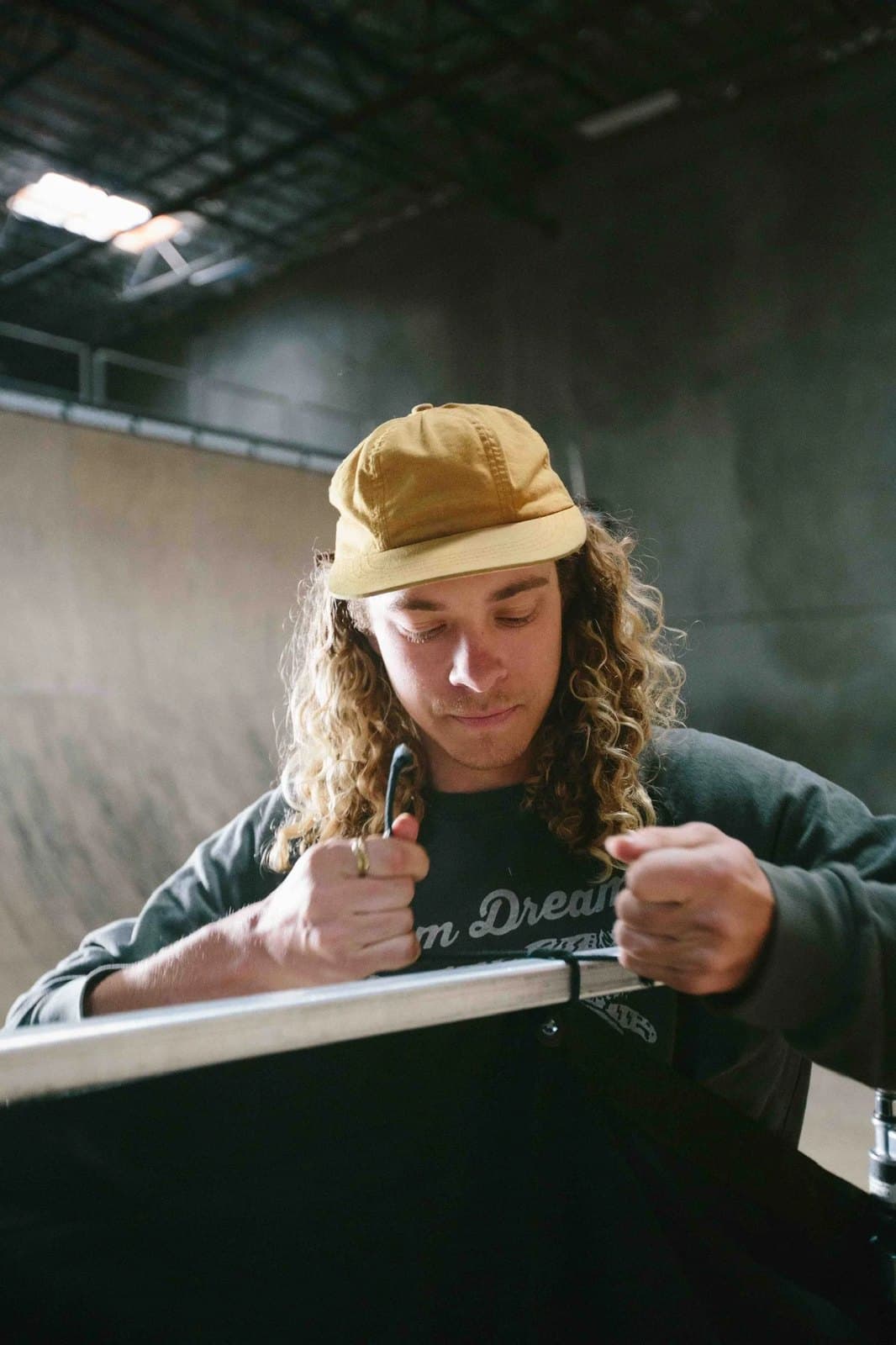 A skater in a yellow cap, sitting at the edge of a ramp.