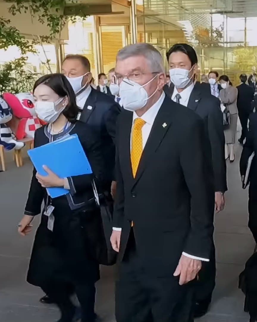 IOC officials in masks walking through a crowd.