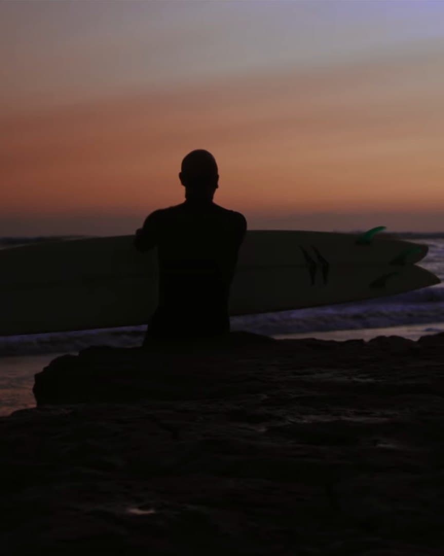 A surfer silhouetted against an ocean sunset.
