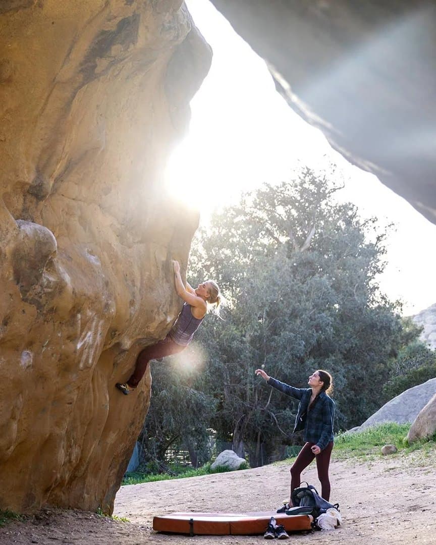 A climber on an overhanging boulder, backlit.